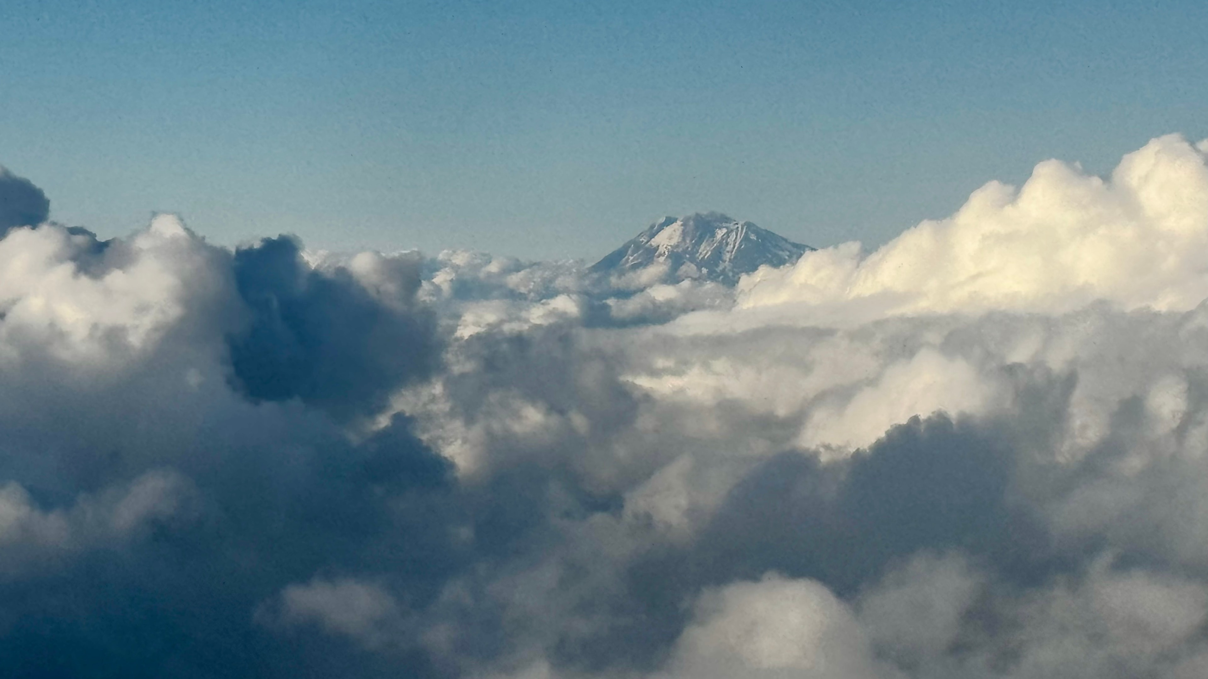 Snow-capped mountain peak rising above a dramatic sea of clouds from aerial view