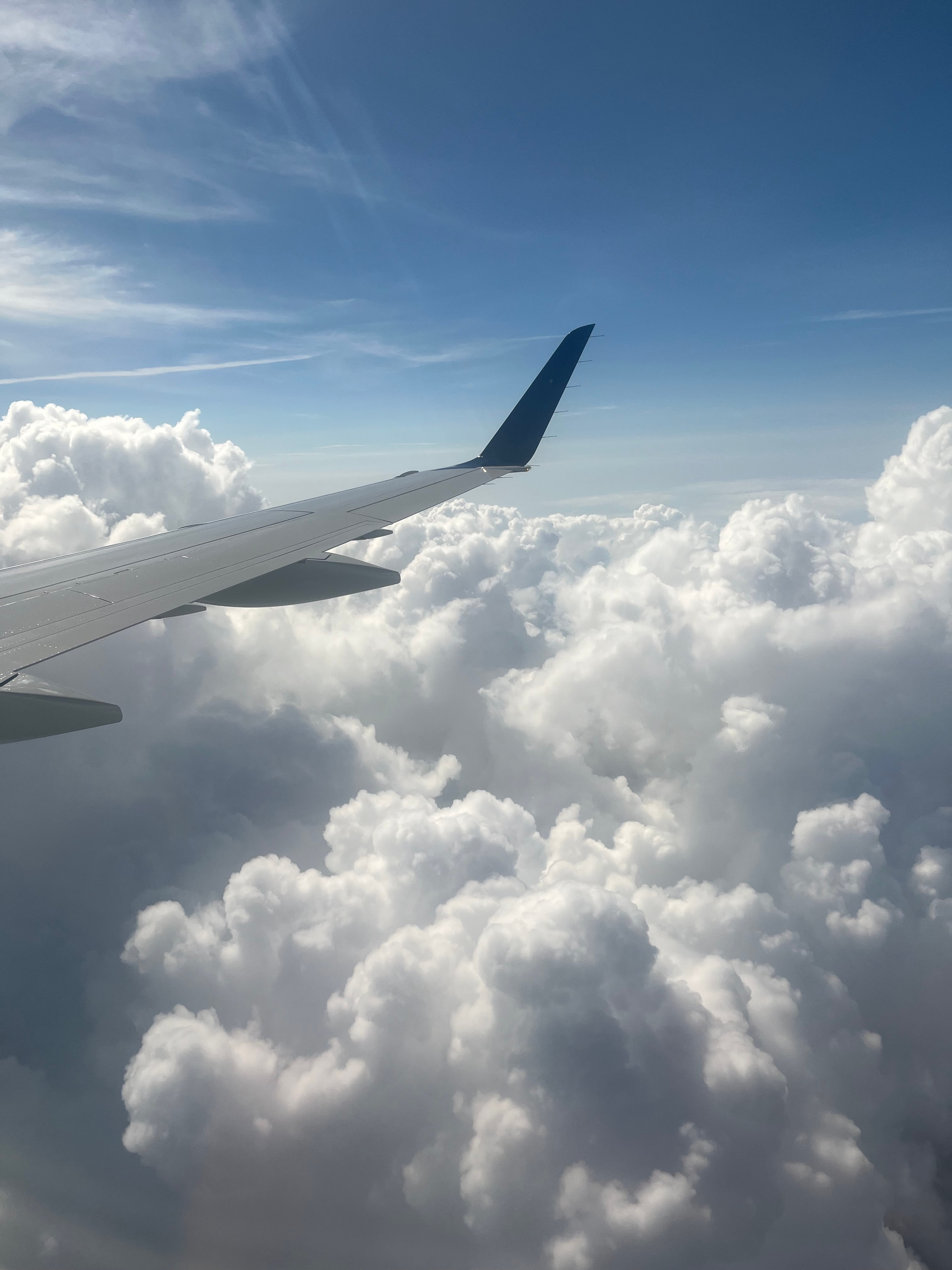 Aircraft wing tip against bright blue sky and billowing clouds