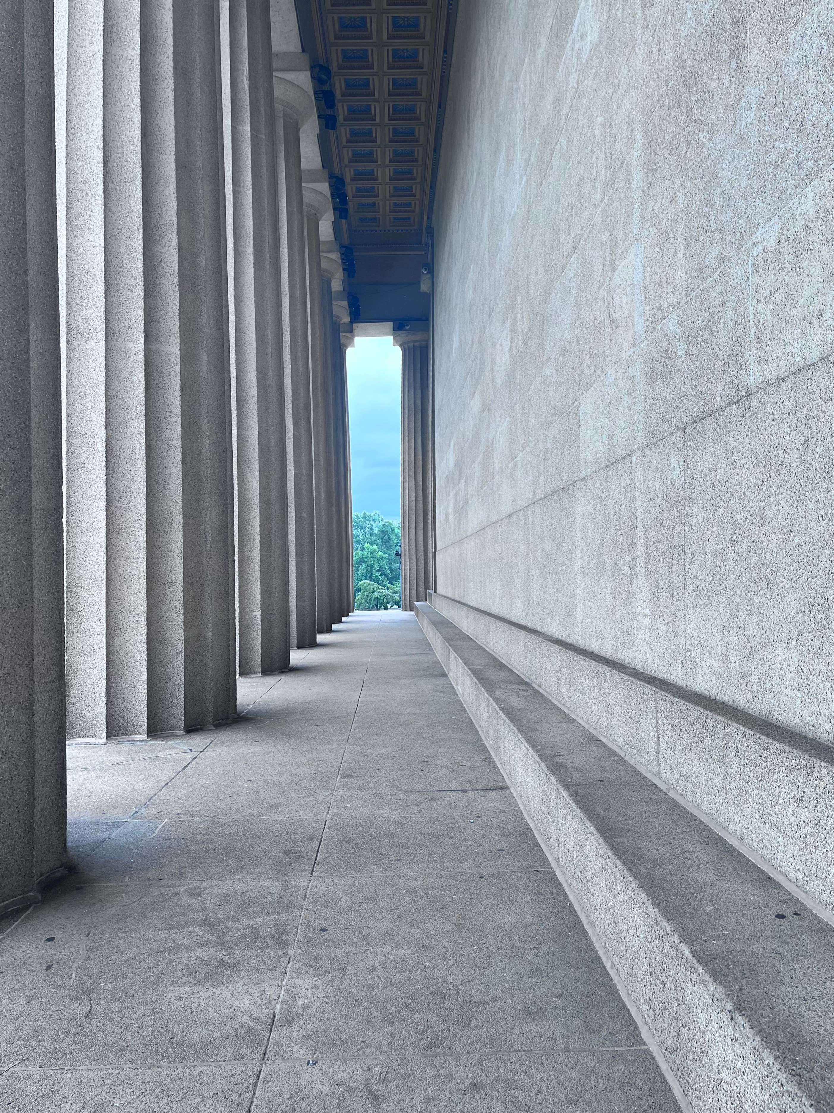 Colonnaded corridor of a classical stone building with blue sky at the end