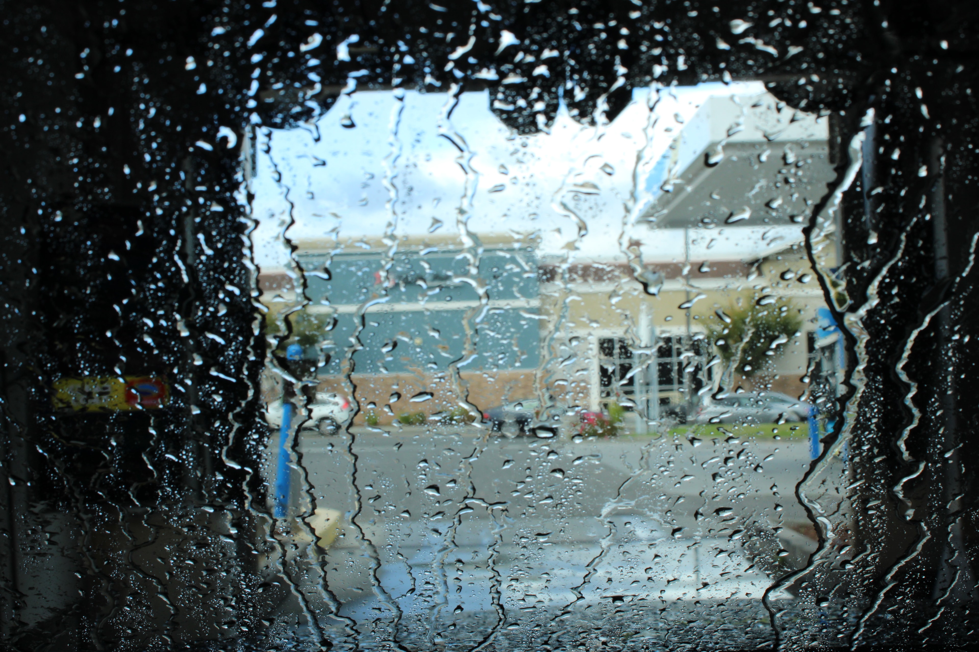View through a rain-streaked car wash window onto a parking lot
